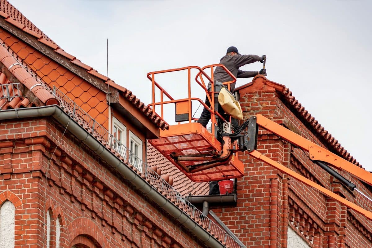 Dachdecker in einer Hubarbeitsbühne am Schornstein eines Backsteinhauses