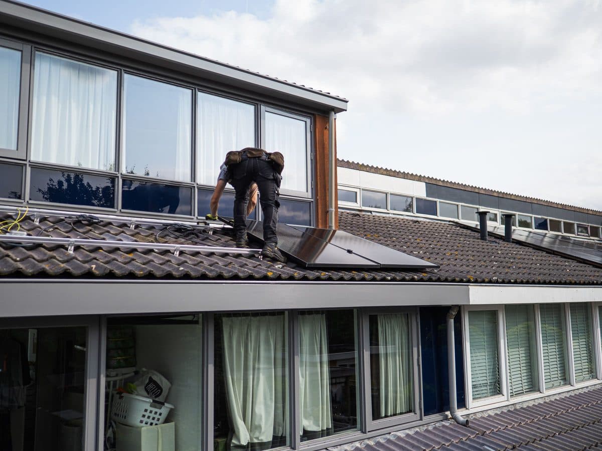 Monteur bringt auf einem Ziegeldach ein Solarmodul an, Aufnahme von hinten